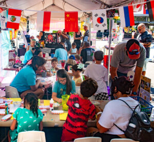 Photo of families creating free art activities under a tent with international flags