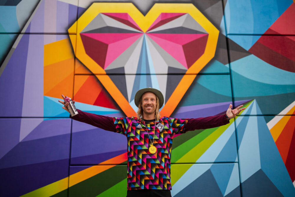 Artist Pat Milbery standing in front of a colorful heart mural