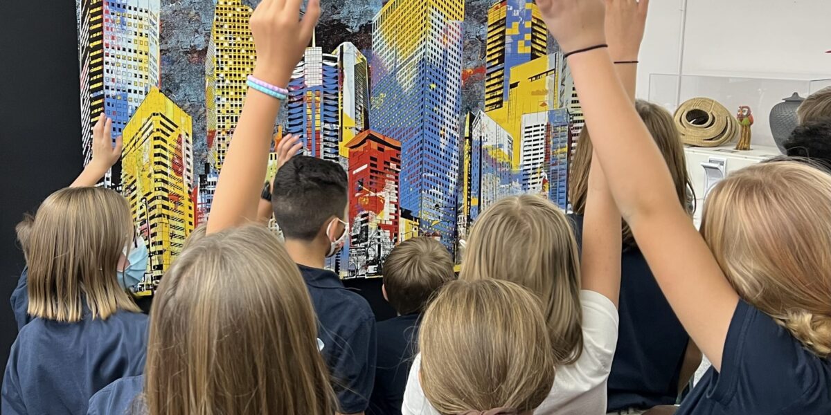 students raising hands looking at artwork