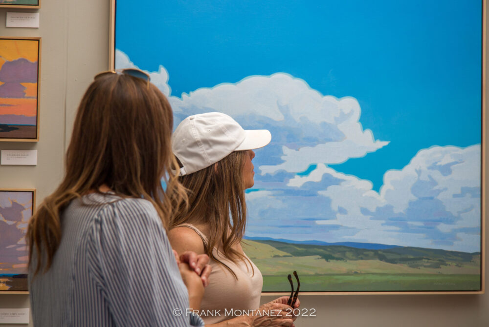 Two women looking at landscape art with clouds and blue sky