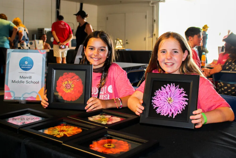 Two students smiling and holding flower artwork